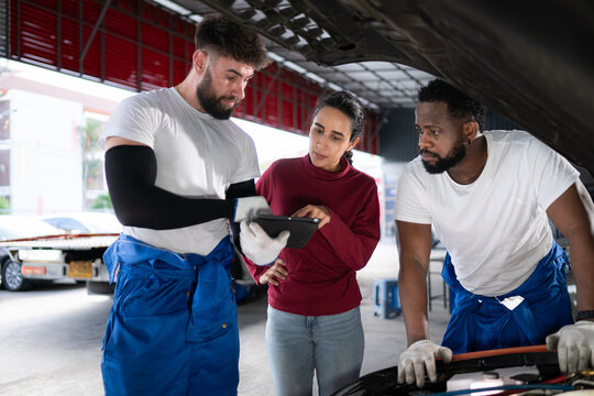 In an auto repair shop, A man professional auto mechanic briefs a female customer about the cost of car repairs and collects payment.