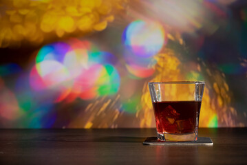 Glass of whiskey on the bar in front of the blur image Christmas background. Festive abstract background with bokeh defocused lights and stars