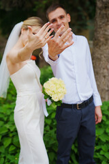 Gentle and happy newlyweds show wedding rings on hands on a walk in the park.