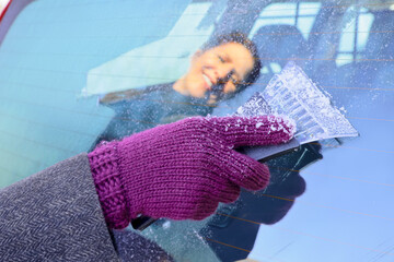 Winter Driving - A cheerful woman is scraping the ice off the frozen windows of her car