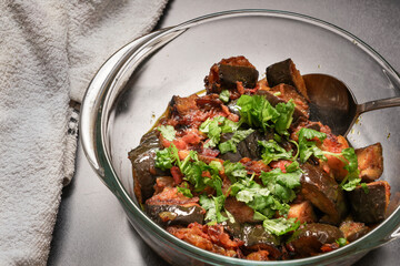 Freshly prepared homemade, delicious traditional spicy aubergine or eggplant curry with onion and tomato, garnished with coriander, served in a glass bowl.