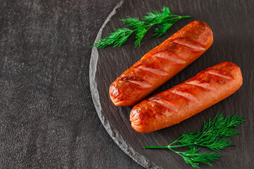 Grilled sausages on plate with dill sprigs, on dark slate stone plate, selective focus