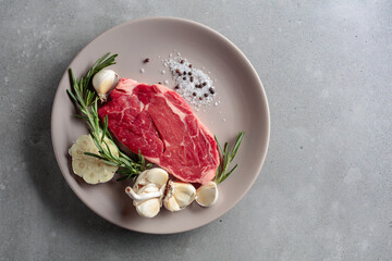 Raw beef steak with rosemary, garlic, salt, and pepper.