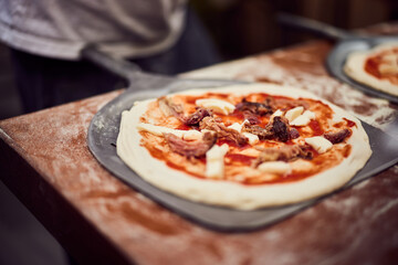 Focus on the freshly made pizza, on the pizza shovel, ready to go into the oven.