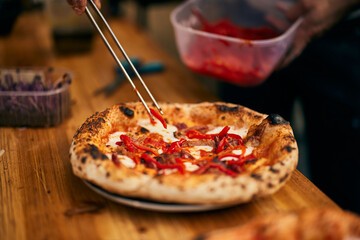 The pizza maker puts slices of red peppers on the baked pizza. - obrazy, fototapety, plakaty