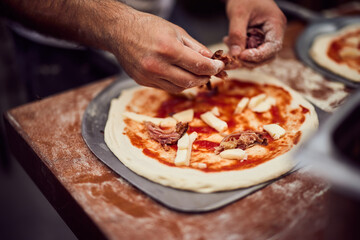 The male hands put ingredients on the pizza dough, preparing it on the pizza shovel.