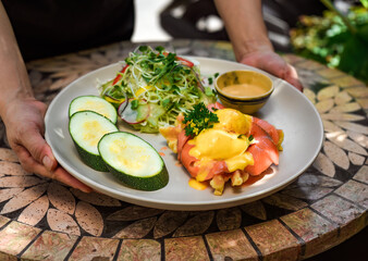  waitress serving a plate with eggs bennedict waffles with smoked salmon in restaurant