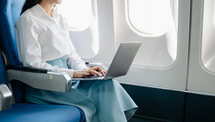 Asian executive excels in first class, multitasking with digital tablet, laptop. Travel in style, work with grace..