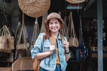 Fototapeta premium Asian tourist girl shopping, walking in famous local street market looking at beautiful straw hats, happy shopping at local market on weekend.