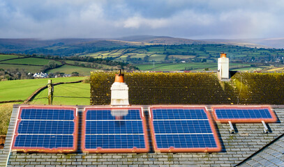 Solar panels on a roof looking out over a rural setting. A soft orange glow has been used to...