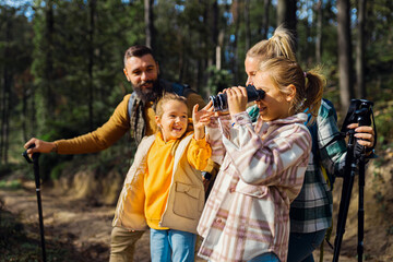 Smiling family of four enjoying hiking in trough forest using binoculars.
