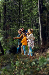 Smiling family of four enjoying hiking in trough forest using binoculars.