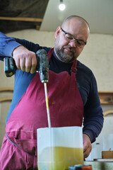 Man stirs epoxy, a process in creating durable finishes. Symbolizes the DIY culture's embrace of...