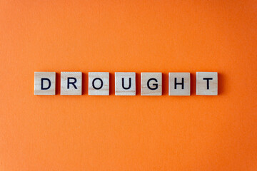 Drought word. The phrase is laid out in wooden letters top view. Orange flat lay background