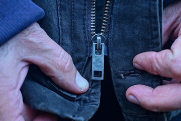fastening with two hands an iron old industrial zipper in a stylish classic fashionable brown fabric warm autumn jacket on the street during the day © FEDOR