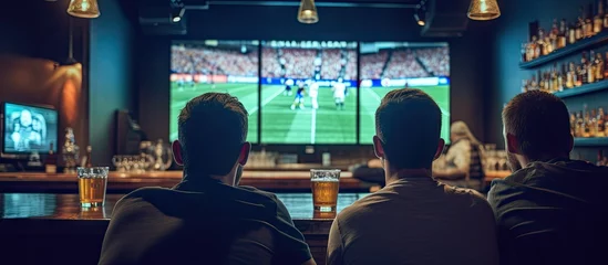 Foto op Plexiglas Friends in sports bar watching game on screens from behind Copy space image Place for adding text or design © Ilgun