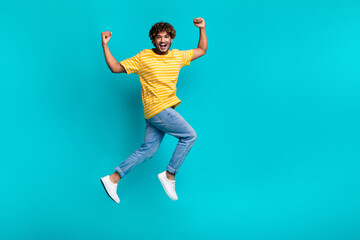 Fototapeta na wymiar Full length photo of delighted crazy handsome guy raise fists success jump run empty space isolated on teal color background
