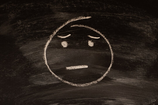 Sad cute emoticon, imoji drawn with chalk on blackboard.