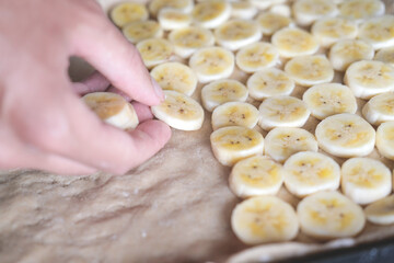 Hand placing sliced banana piaces on dough , closeup, preparing banana pizza