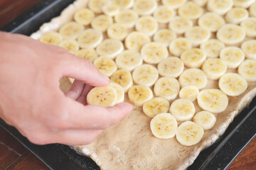 Hand holding a banana slice and put it on the dough while making banana pizza