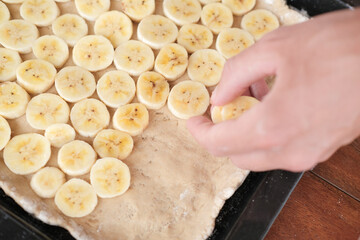 Hand puts banana slices on dough, close up