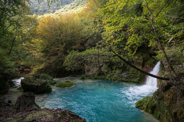 Paisaje otoñal en el nacedero del Urederra, sierra de Urbasa, con cascada y un bosque de hayas, Navarra, España.