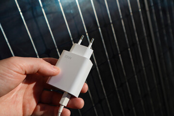 Charger for mobile devices in hand on the background of a solar panel. The concept of green...