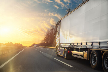 Tail view white blank modern delivery big shipment cargo commercial semi trailer truck moving motorway road city urban suburb. Business distribution logistics service. Lorry driving highway sunset