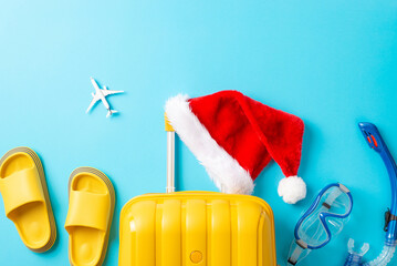 Explore islands for a festive New Year! Capture the essence with a top-view shot of a suitcase, Santa hat, snorkeling gear, miniature plane, sandals on a vibrant blue backdrop