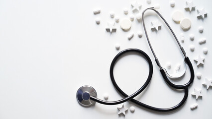 Christmas medical banner. Close-up of stethoscope, stars and pills on white background, top view, flat lay, copy space. New Year's medicine, congratulations to doctor.