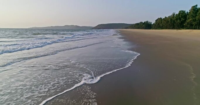 Cinematic aerial shot of flying close on the crashing waves on the empty beach coastline