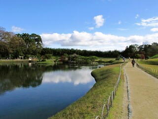 Woman on a path next to Lake with clear reflection of blue sky and clouds, representing: future, journey, satisfaction, retirement, peaceful life