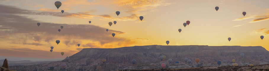 A panorama of hot air balloons in the sky at dawn against the backdrop of mountains. Breathtaking colors fill the sky.