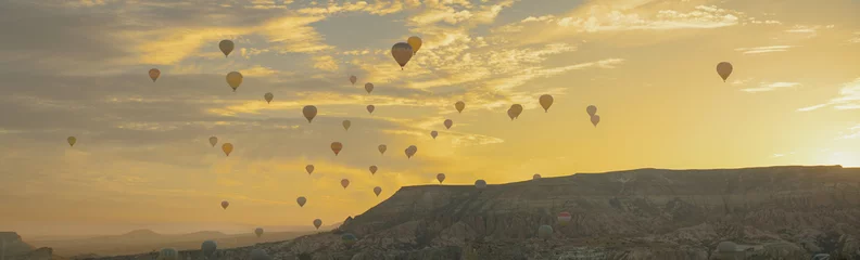 Papier Peint photo Lavable Ballon The valley with hot air balloons at sunrise amid the rocks, the sun rising from behind the mountains painted the clouds in golden color, Cappadocia, Turkey.