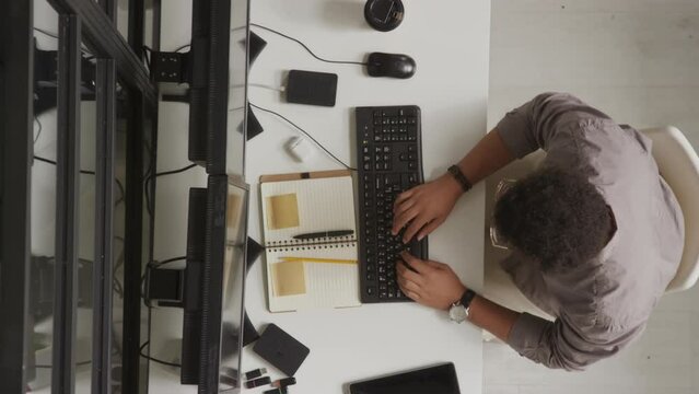 Top view stab shot of Biracial male programmer typing html code in computer while sitting in front of two monitors at work desk in office