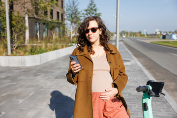 Woman unlocks an e-scooter with his mobile phone. Electric scooter new way city mobility. Green transportation. Sustainable climate neutral cities goals. Green mobility sustainable transportation