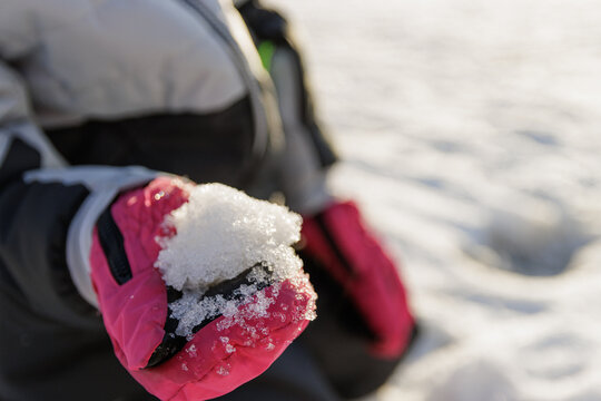 Close up image of child's hands with snow gloves scooping up snow