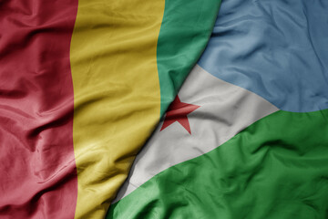 big waving national colorful flag of guinea and national flag of djibouti .