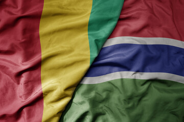big waving national colorful flag of guinea and national flag of gambia .