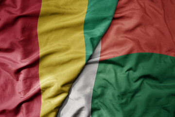 big waving national colorful flag of guinea and national flag of madagascar .
