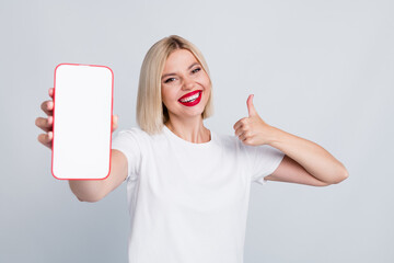 Portrait of toothy beaming girl with bob hairstyle wear white t-shirt show smartphone display thumb...