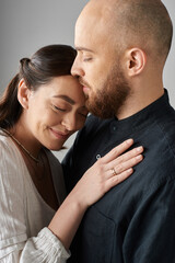 vertical shot of joyful beautiful couple hugging warmly in stylish outfits on gray backdrop