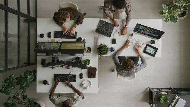 Top view of multiethnic programmers team program coding and coworking while sitting at white desk in minimalist open space officeTop view of multiethnic programmers team program coding and coworking w
