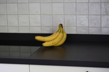 A portrait of a bunch of yellow bananas with som brown spots lying on a black kitchen countertop. The delicious energizing food is ready to eat and ideal before a sport activity.