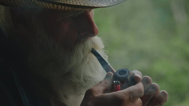 Close up of elderly man lightning smoking pipe while relaxing in nature