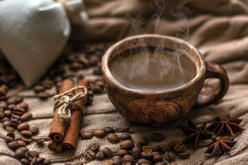 Hot coffee in a coffee cup and many coffee beans placed around on a wooden table in a warm, light atmosphere, on dark background, with copy space.