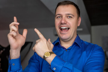 Happy man in a blue shirt shows his hands to the side indoors