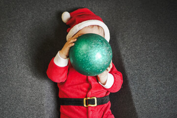 happy smiling baby boy in red santa claus costume with christmas hat playing with christmas balls...