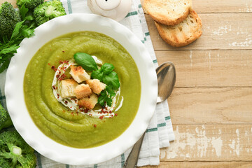 Broccoli cream soup. Fresh homemade broccoli soup in white plate with seasonings, parsley, basil and pieces of toasted bread on rustic white wooden background. Healthy, diet or baby food. Top view.