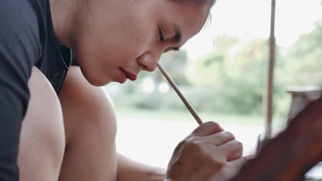 Close-up of Asian woman painter creating art use a paintbrush to draw lettering designs on a wooden coffee shop sign. outdoor activities, People doing activities.4k